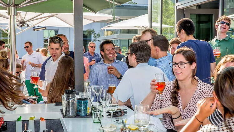 A wide shot of people socializing and holding drinks at an outdoor patio gathering