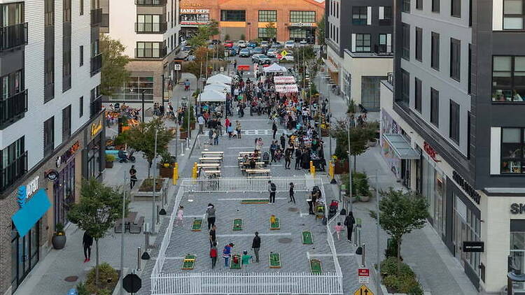 A wide shot of people gathering and playing lawn games on a pedestrian street in an urban area