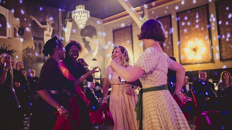A wide shot of people dancing at a party in a decorated ballroom.