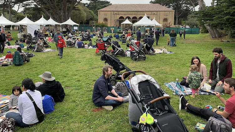 A wide shot of families gathering on a lawn at an outdoor event. A wide shot of families gathering on a lawn at an outdoor event.
