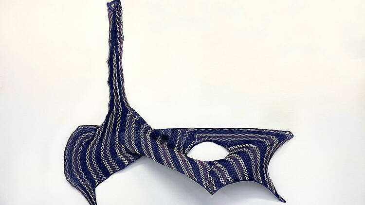A close-up of a blue patterned sculpture displayed on a white wall.