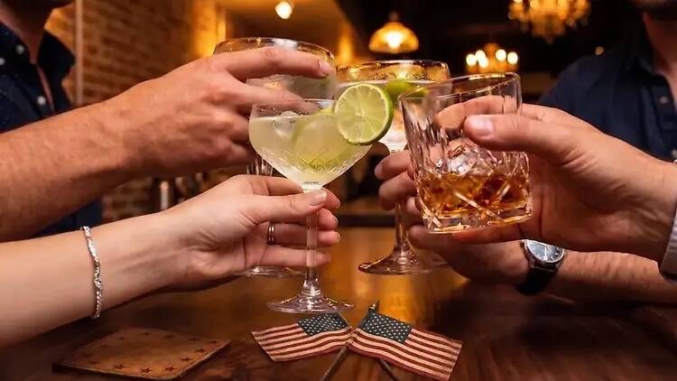 A close-up of people clinking drinks at a bar. A close-up of people clinking drinks at a bar.