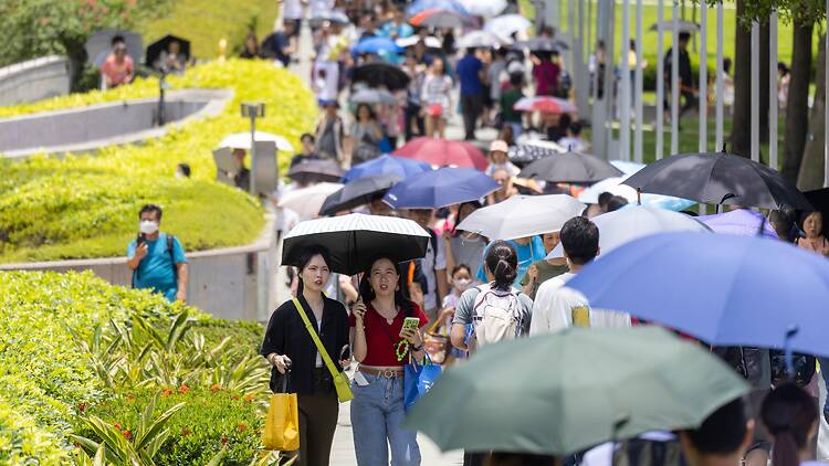 Tourists walking with umbrellas in Hong Kong hot summer heat