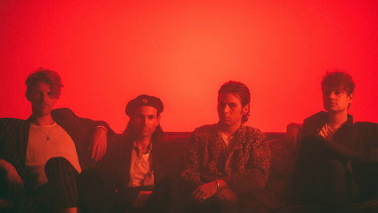 A wide shot of four people sitting together on a couch in a red-lit room.