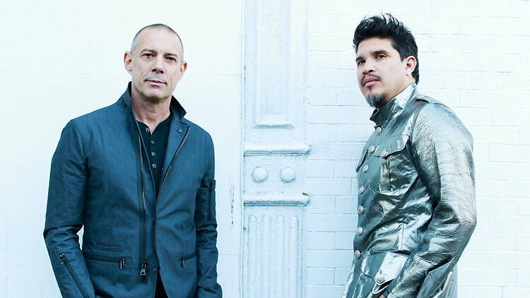 A wide shot of two people standing against a white brick wall