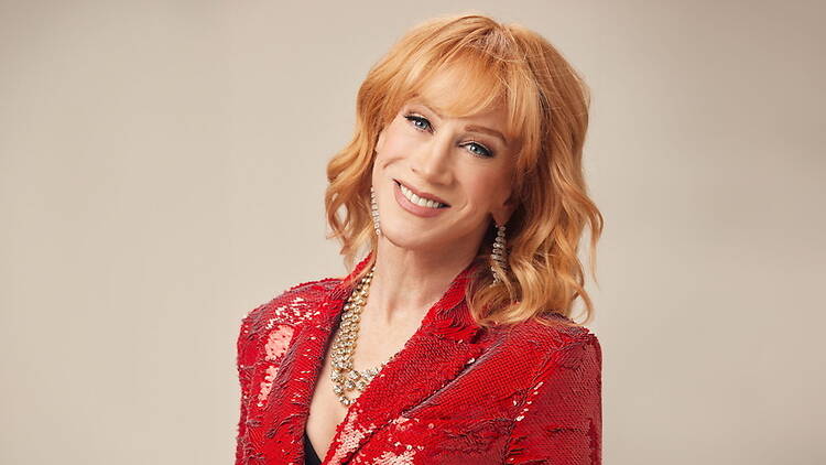 A close-up of a person smiling in a red sequined jacket against a beige background