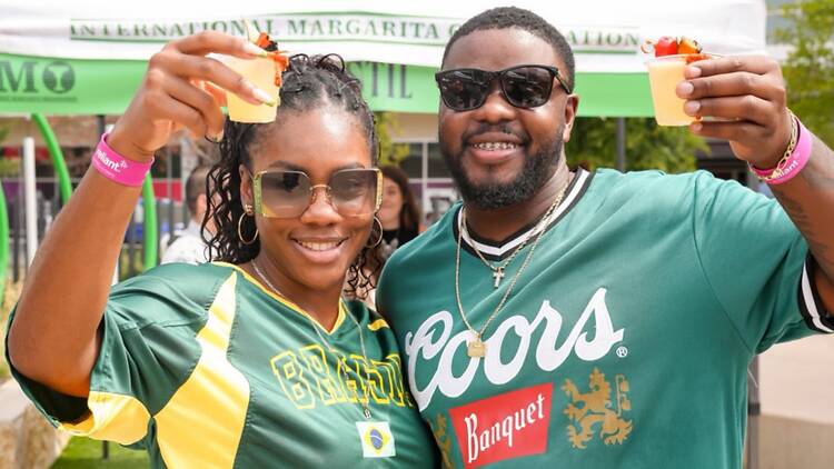 A wide shot of two people raising drinks outdoors.