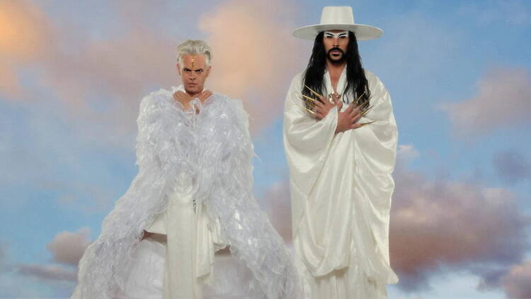 A wide shot of two people dressed in white standing against a cloudy sky backdrop A wide shot of two people dressed in white standing against a cloudy sky backdrop