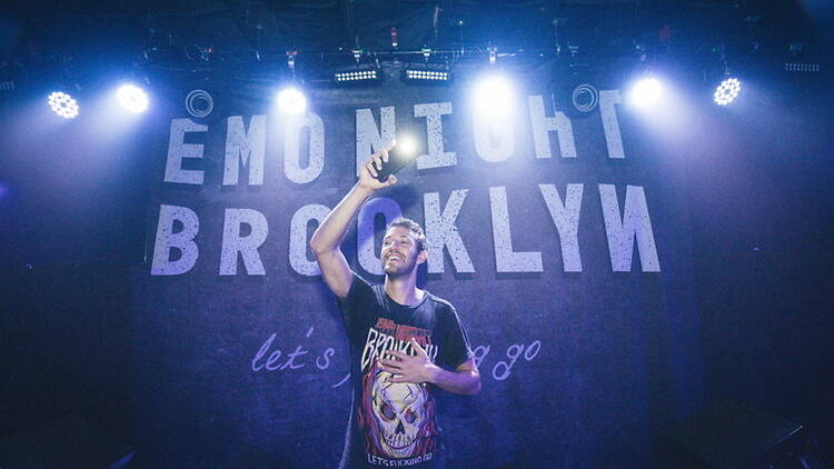 A wide shot of a person holding a microphone on a stage beneath concert lights A wide shot of a person holding a microphone on a stage beneath concert lights