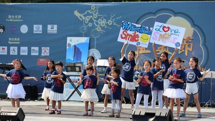 A wide shot of children performing on stage while holding signs at an Asian Pride event.