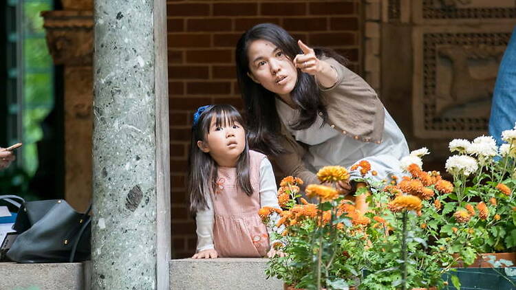 Close-up of a person pointing toward flowers beside a child in a garden courtyard
