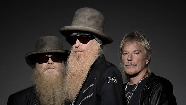 A close-up of three people wearing hats and sunglasses against a dark backdrop