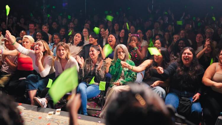 A wide shot of a crowd cheering and waving green flags at an event.