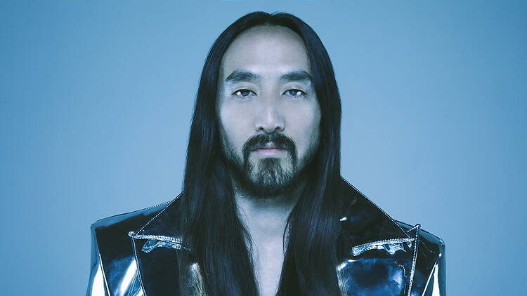 A close-up of a person posing in a metallic jacket against a blue backdrop.
