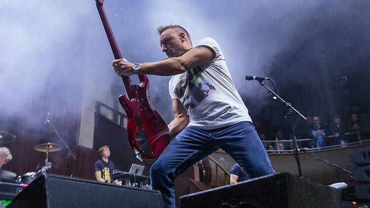 A wide shot of a person playing a red guitar on stage during a live performance.