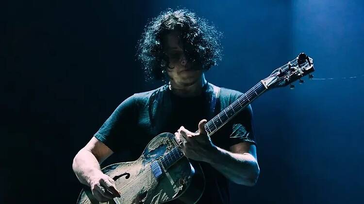 A close-up of a person playing an acoustic guitar under blue stage lights.