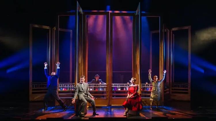 A wide shot of five people performing on a theater stage under colorful lights.