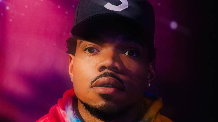 A close-up of a person wearing a cap and hoodie under pink and purple lights.