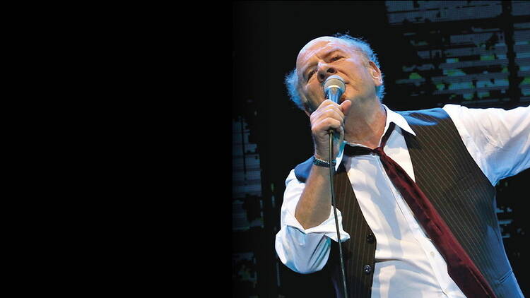 A close-up of a person singing into a microphone on stage.