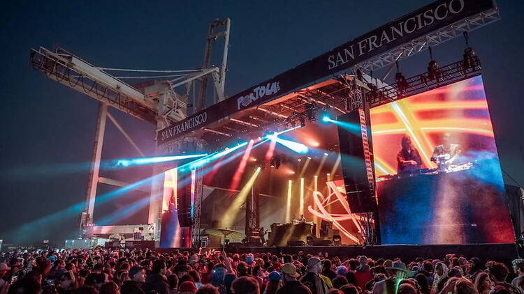 A wide shot of a crowd watching a live music performance on an outdoor stage.