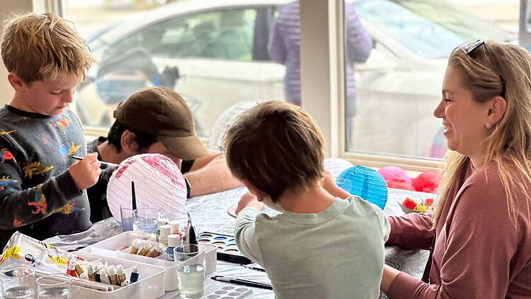 A wide shot of children doing arts and crafts with an adult at a table indoors.