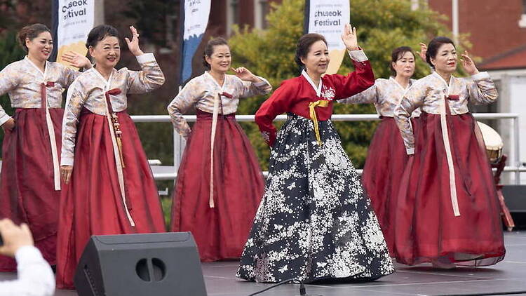 A wide shot of women performing a traditional dance on an outdoor stage.
