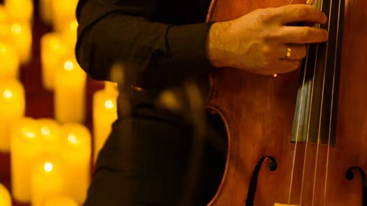 A close-up of a person playing a cello surrounded by warm candlelight.