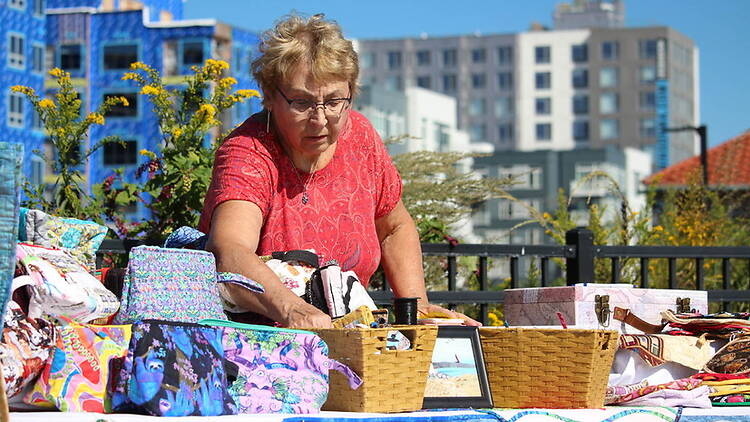 A wide shot of a person arranging handmade items at an outdoor market stall.