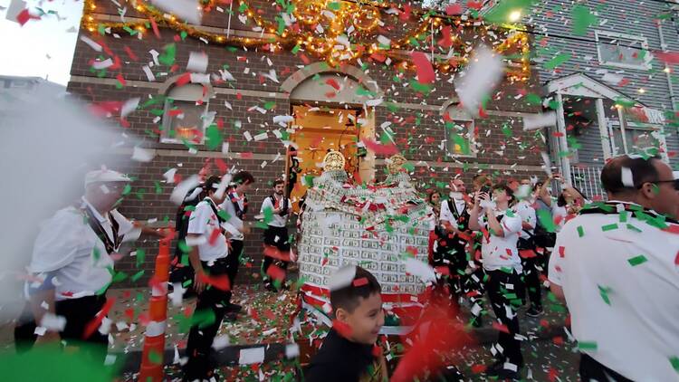 A wide shot of people celebrating in costume as confetti falls outside a decorated building.