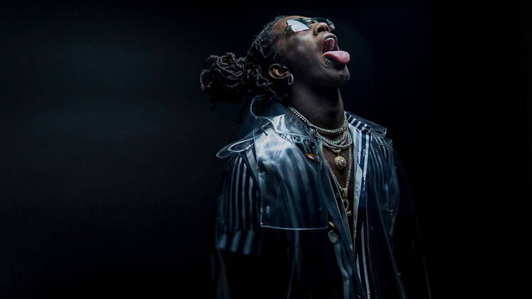 A close-up of a person posing in a leather jacket under dark lighting.