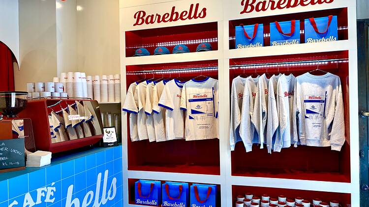 Interior of a Café Barebells pop-up store displaying branded apparel, merchandise, mugs, and protein bars next to a coffee counter.