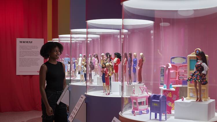 Woman looks at different Barbie dolls in glass cases at an exhibition.