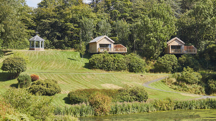 The Huts are custom-built, timber-clad retreats set high on the grassy slopes overlooking the valley and lakes, featuring private outdoor decking and sunken copper bath tubs. To the far left, you can also see one of the estate's garden gazebos.