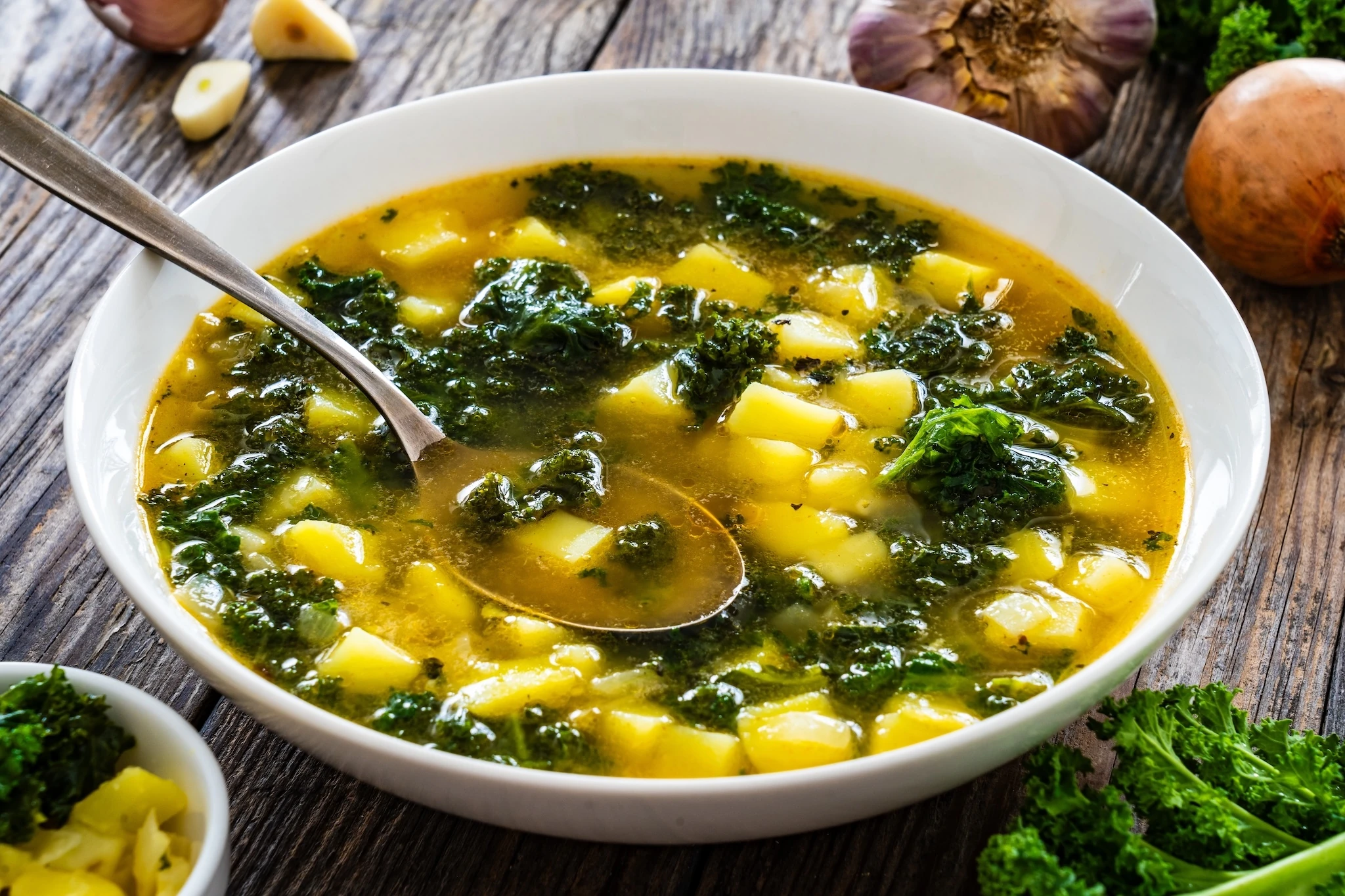 Portuguese green soup - Caldo Verde. Potato and kale soup served in white bowl on wooden table