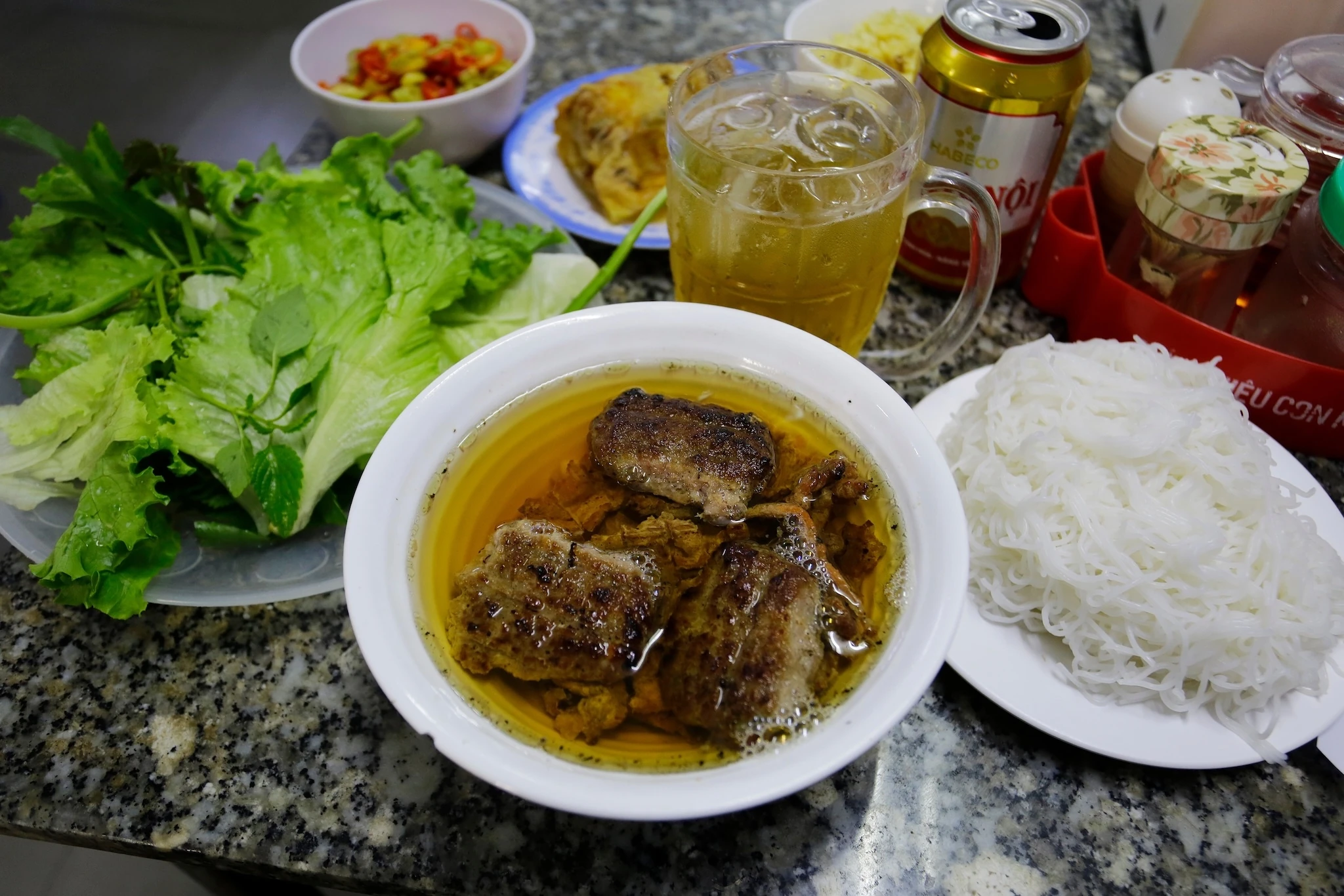 Bun Cha, a Vietnamese dish of grilled caramelized pork, noodles and fresh herbs, is served at Bun Cha Huong Lien restaurant. Glass of cold local beer with ice is seen.