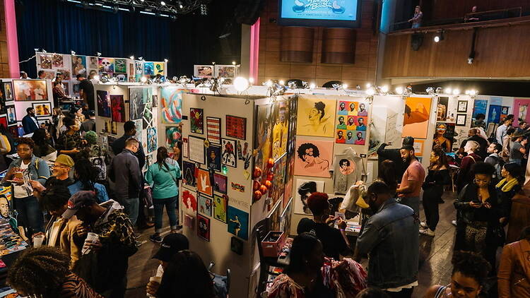 A wide shot of a crowd browsing artwork at an indoor art festival. A wide shot of a crowd browsing artwork at an indoor art festival.