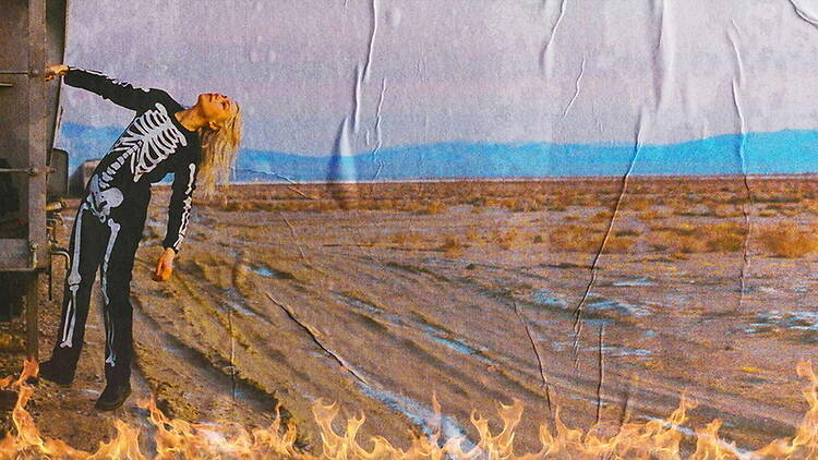 A wide shot of a person in a skeleton costume posing in front of a landscape backdrop with flames. A wide shot of a person in a skeleton costume posing in front of a landscape backdrop with flames.