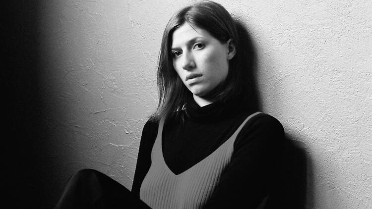 A close-up of a person sitting against a wall in a black-and-white portrait.