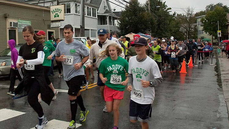 A wide shot of participants running in a road race along a city street on a rainy day A wide shot of participants running in a road race along a city street on a rainy day