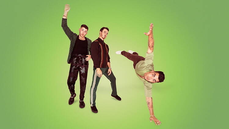 A wide shot of three performers posing and dancing against a green studio backdrop