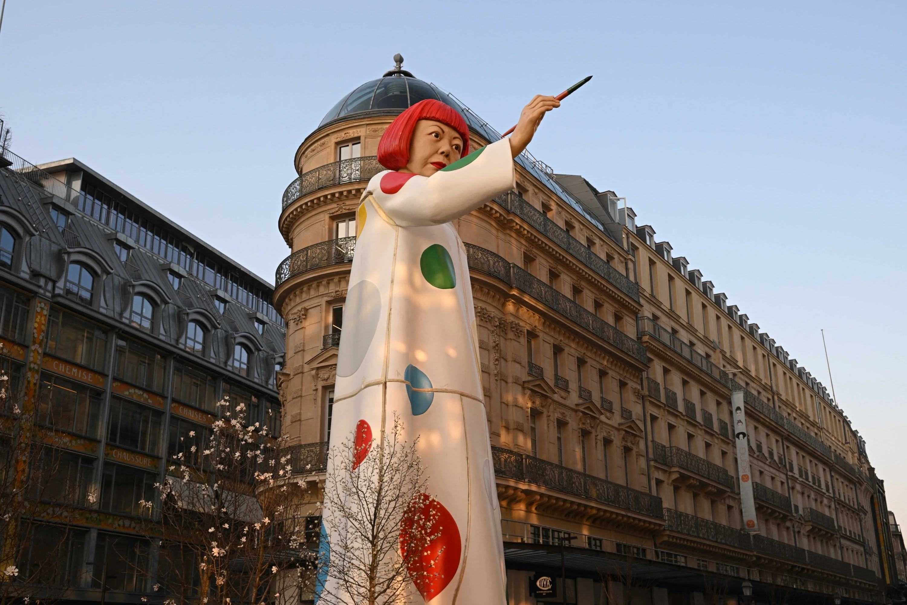 Large statue depicting Japanese artist Yayoi Kusama pointing a paintbrush towards Louis Vuitton headquarters in Paris (2023)