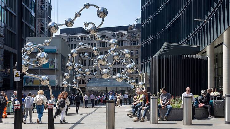 People are walking and sitting near a modern sculpture in a city. Infinite Accumulation by Yayoi Kusama People are walking and sitting near a modern sculpture in a city. Infinite Accumulation by Yayoi Kusama