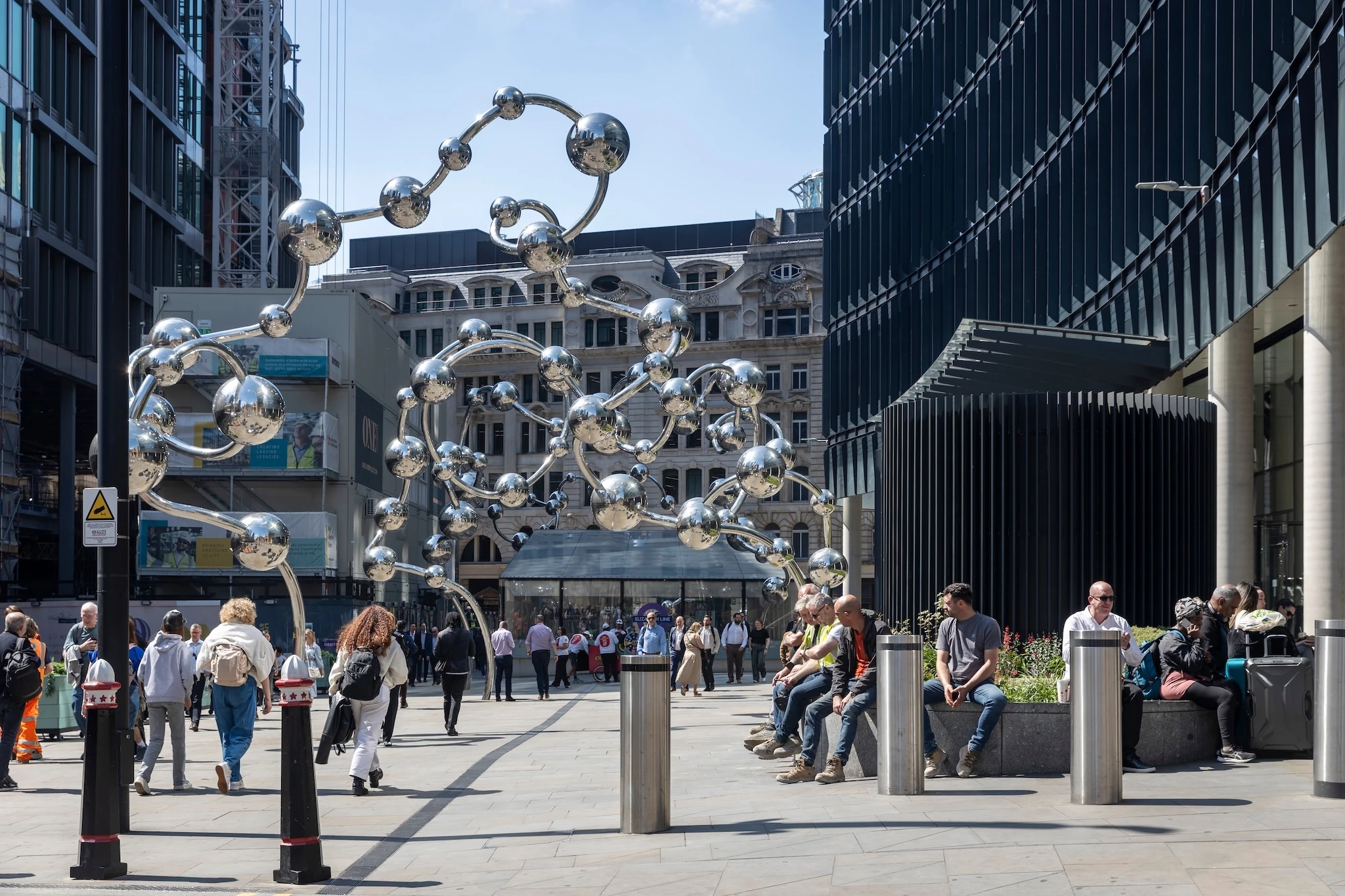 People are walking and sitting near a modern sculpture in a city. Infinite Accumulation by Yayoi Kusama