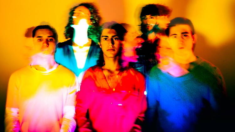 A wide shot of five band members posing together under colorful studio lighting A wide shot of five band members posing together under colorful studio lighting