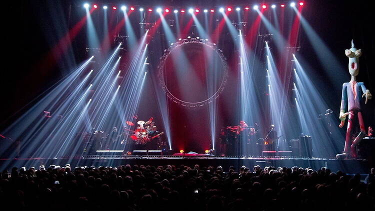 A wide shot of musicians performing on a brightly lit concert stage before an audience A wide shot of musicians performing on a brightly lit concert stage before an audience