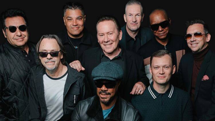 A wide shot of band members posing together against a dark studio backdrop A wide shot of band members posing together against a dark studio backdrop