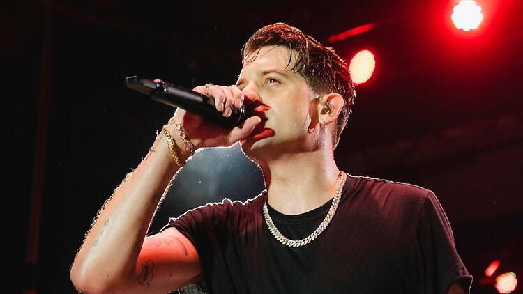 Close-up of a singer performing into a microphone on a concert stage under red lighting