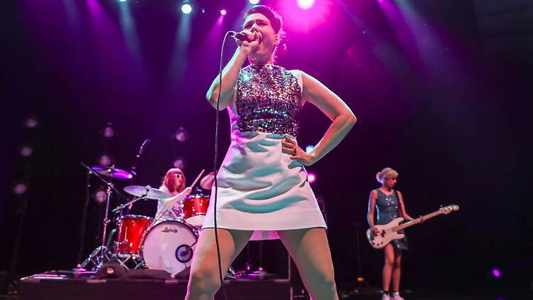 A wide shot of a singer performing with band members on a brightly lit concert stage