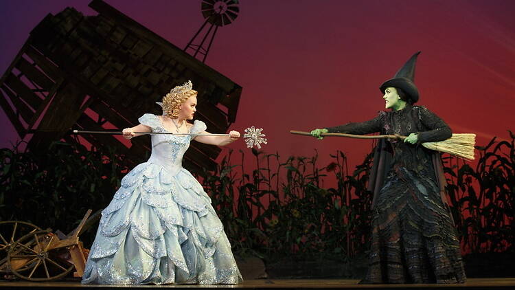 A wide shot of two people performing on stage with a wand and broomstick. A wide shot of two people performing on stage with a wand and broomstick.