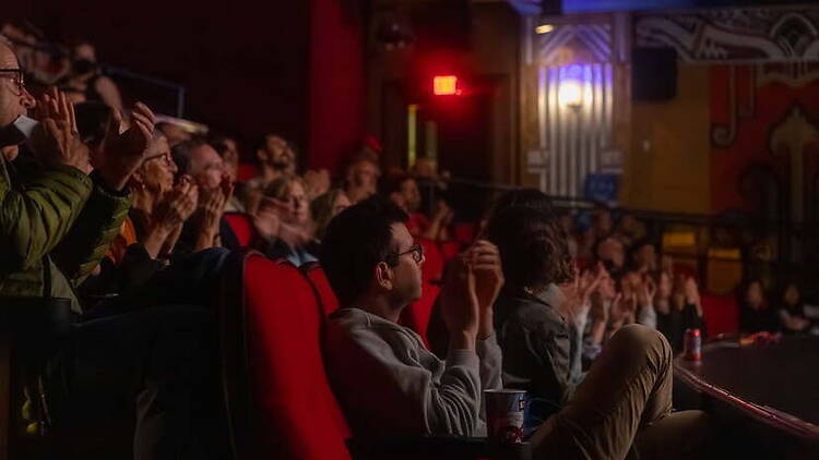 A wide shot of audience members applauding during a live performance in a theater A wide shot of audience members applauding during a live performance in a theater